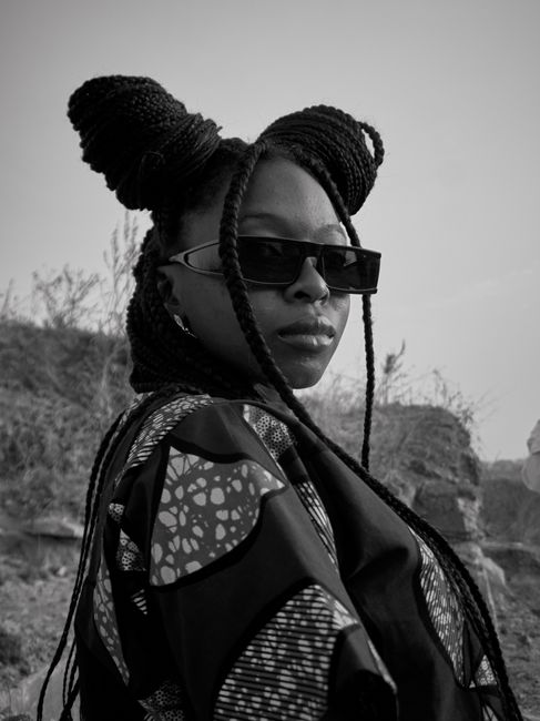Black woman confidently posing with braids and sunglasses outdoors.