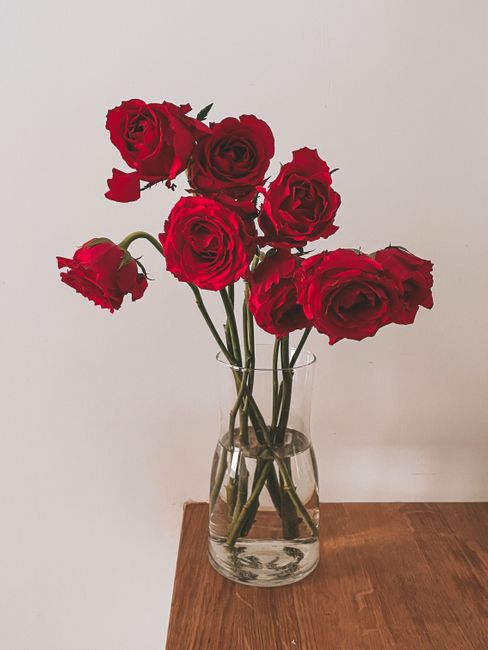 A bouquet of vivid red roses displayed in a clear glass vase on a wooden surface.