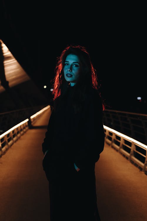 Woman in Coat Standing on Bridge at Night