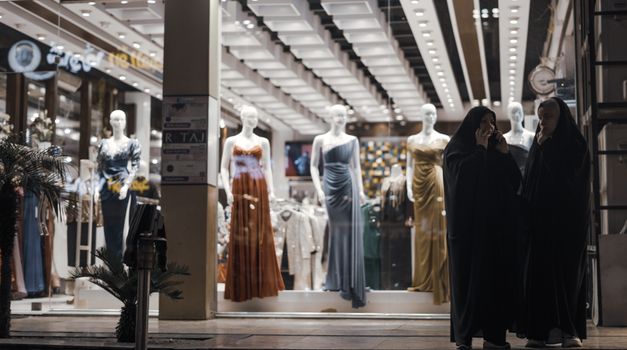 Fashion display with mannequins and shoppers outside a store at night.