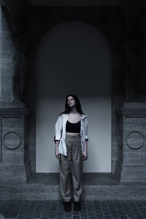 A Woman in White Long Sleeves Standing Beside the Arch Wall