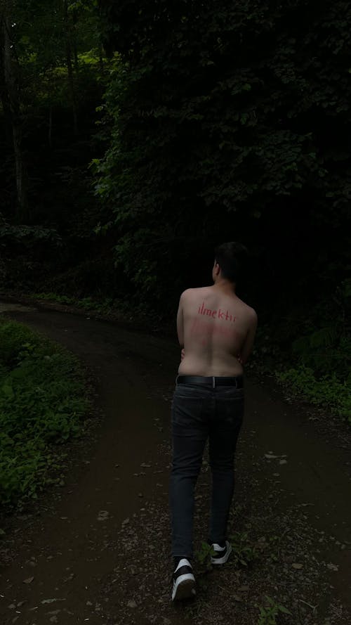 Topless Man in Black Jeans Walking on Unpaved Pathway