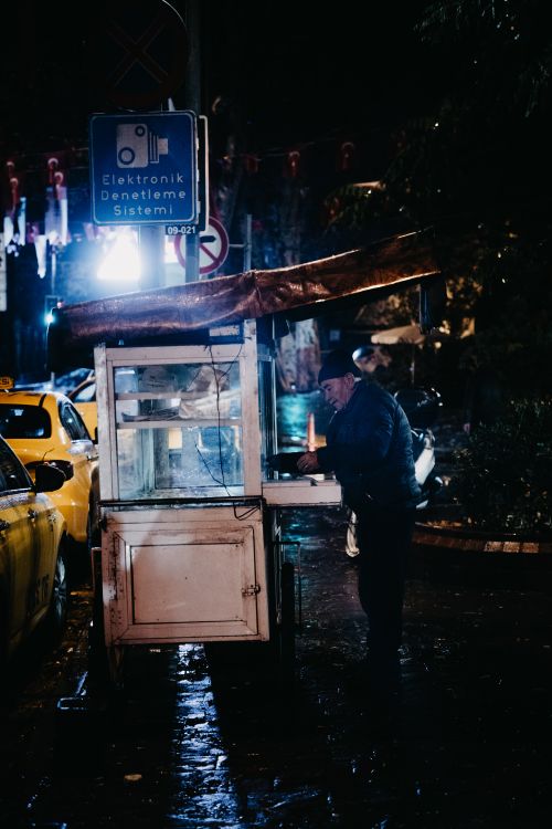Free Elderly man operates a food cart at a bustling nighttime street market. Stock Photo
