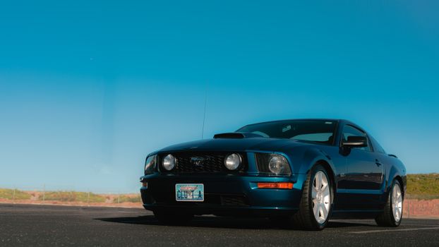 A blue sports car parked on an asphalt road under a clear blue sky, showcasing modern automotive design.