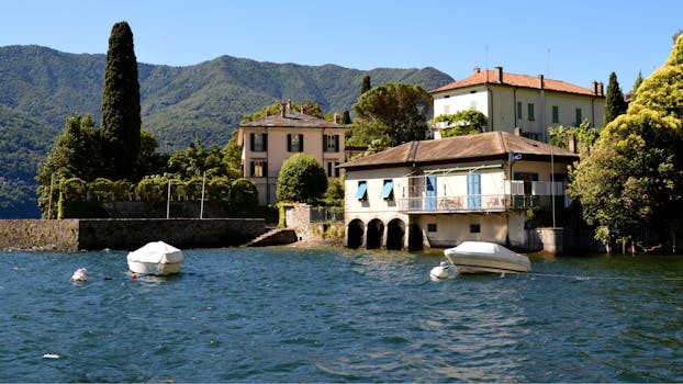 Picturesque villas on an Italian lake with boats and mountainous backdrop.