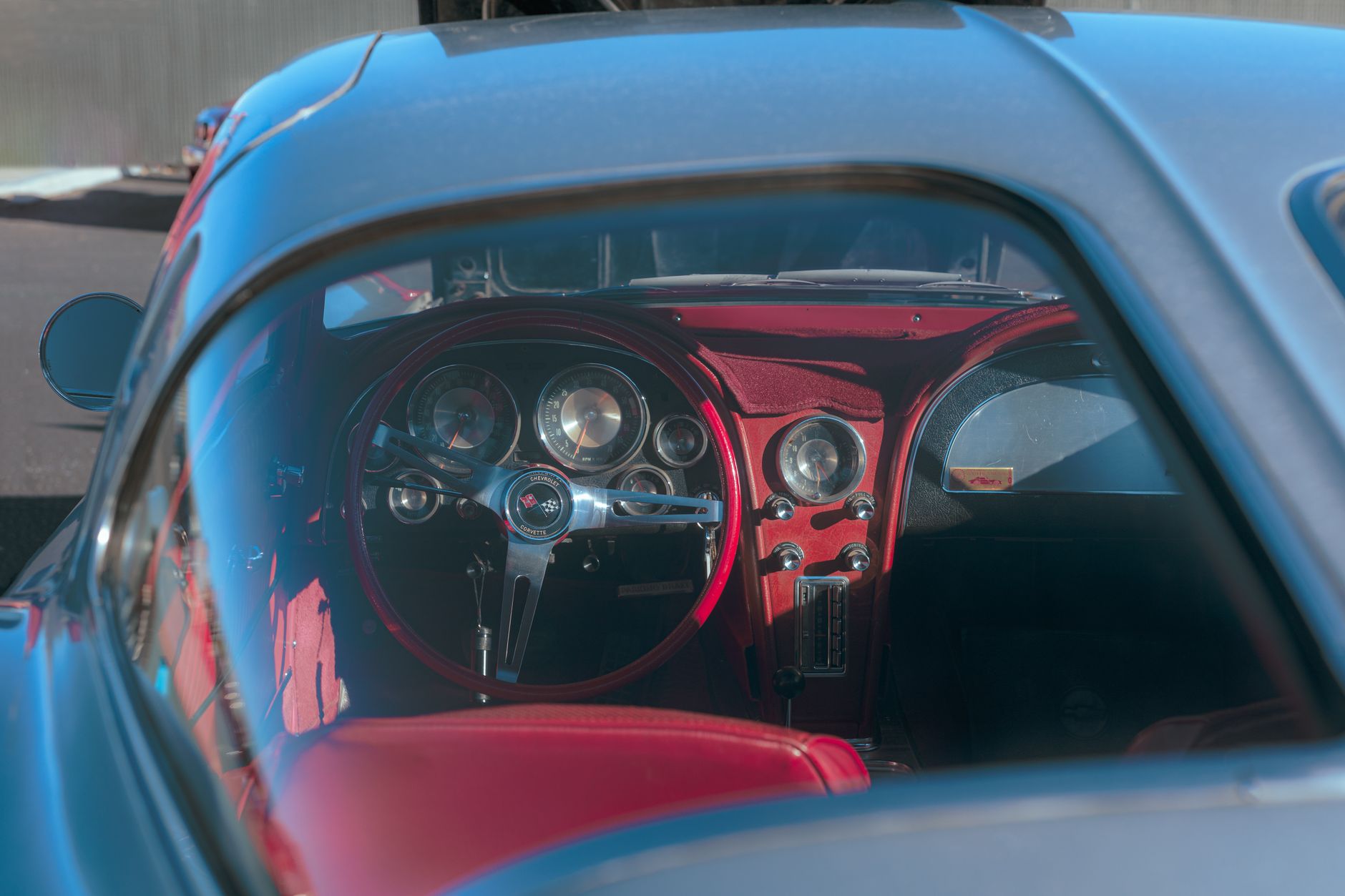 Capture of a vintage Chevrolet Corvette's luxurious red leather interior and glossy steering wheel.