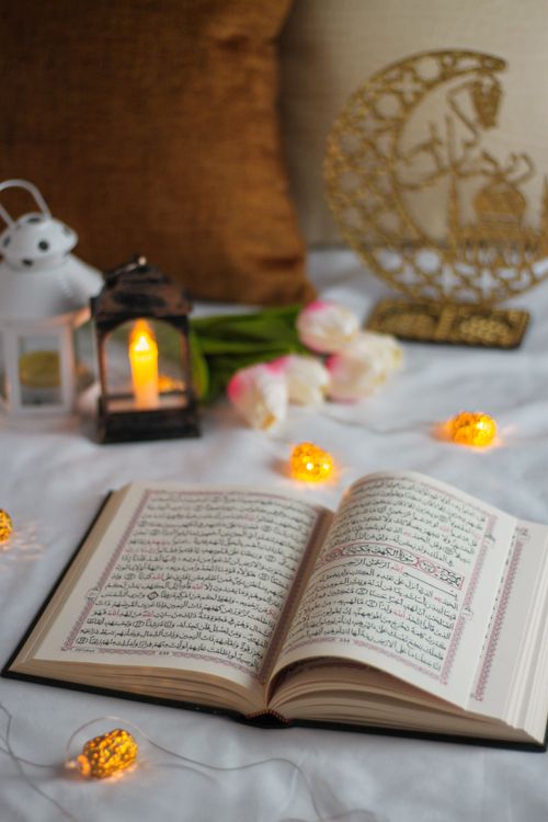 Free Open Quran surrounded by glowing lanterns and decorative objects on a cozy setting. Stock Photo