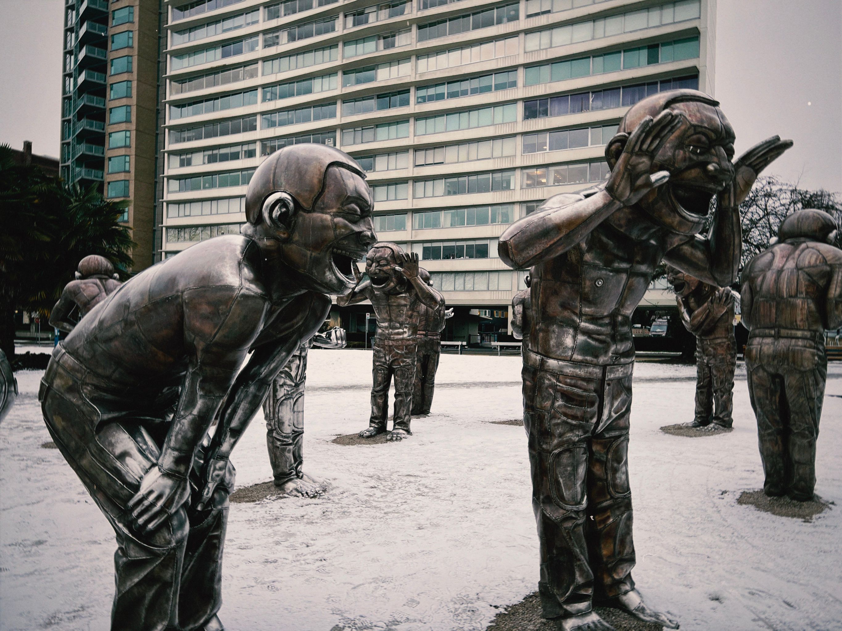 Bronze sculptures laughing in a wintery urban setting with high-rise buildings.