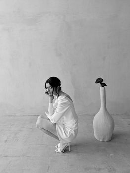 Black and white photo of a woman in a modern studio setting beside a large vase.