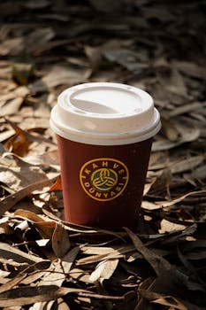 A branded disposable coffee cup sits among fallen leaves, capturing the essence of autumn outdoors.