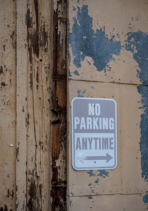 Free A weathered 'No Parking Anytime' sign on a decaying wooden wall with peeling paint. Stock Photo