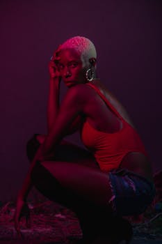 Creative fashion portrait of a woman crouching in vivid lighting, showcasing bold style.