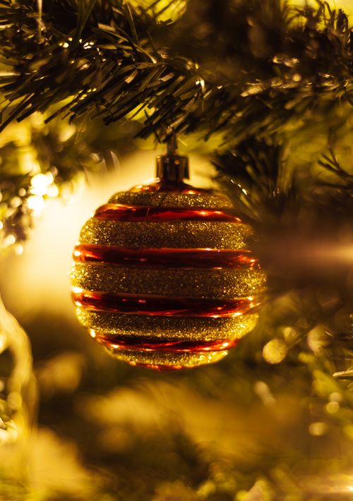 Free A shiny Christmas bauble with gold and red stripes hanging on a festive tree branch, illuminated warmly. Stock Photo