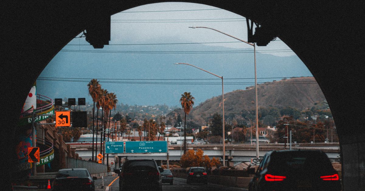 A scenic view from inside a tunnel facing a highway with palm trees and mountains in the background.