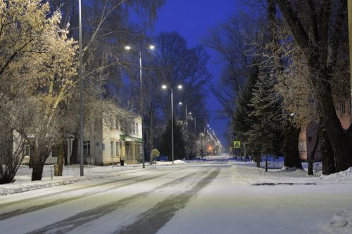 Free A serene winter street at night covered in snow, illuminated by streetlights. Stock Photo