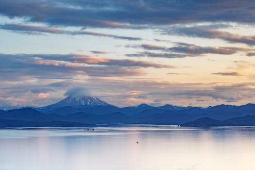 Peaceful scene of mountains and a lake under vibrant, cloudy sky at sunset.