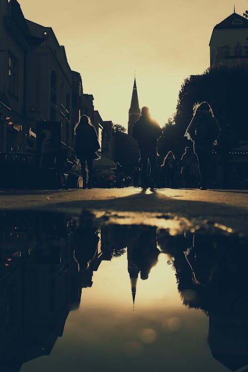 Silhouette of People Walking on Street Reflected on Puddle