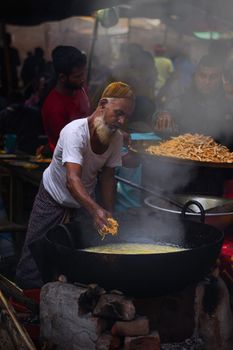 Man cooking traditional street food in a bustling Dhaka market.