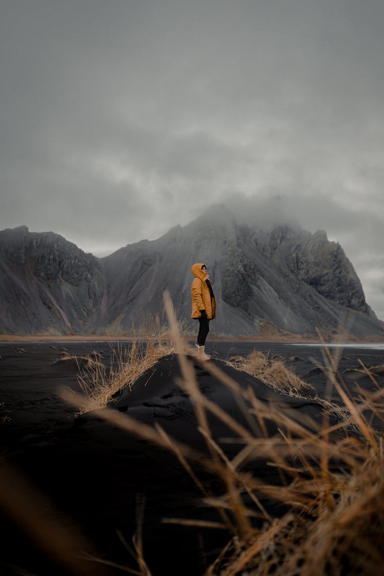 Person In Yellow Jacket Standing On Volcanic Sand In Mountains