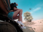 在迪拜沙漠的机械上，一位女子坐在晴朗的天空下观看无人机