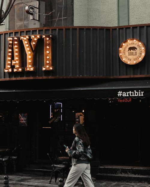 Woman Walking in front of a Bar in City 