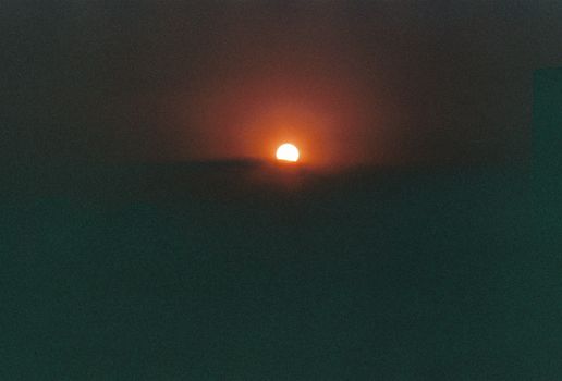 A peaceful sunset casting a warm red glow over the horizon, captured in a minimalist style.