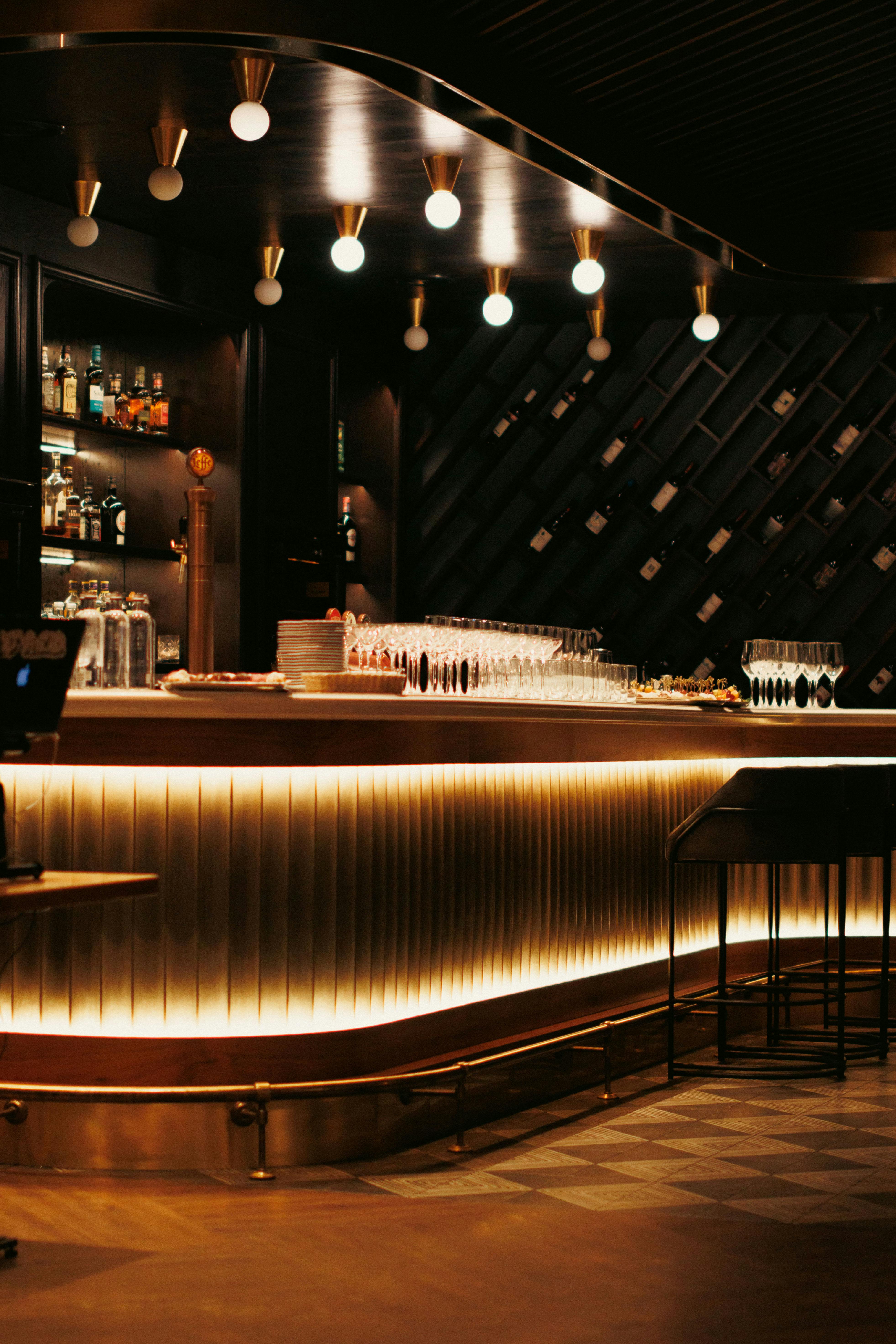 Warm, illuminated luxury bar design with bottles and elegant wine glasses.