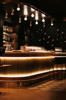 Warm, illuminated luxury bar design with bottles and elegant wine glasses.