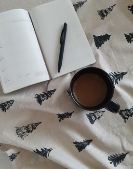 Overhead view of a coffee cup with a notebook and pen on patterned fabric. Perfect for planning or writing.