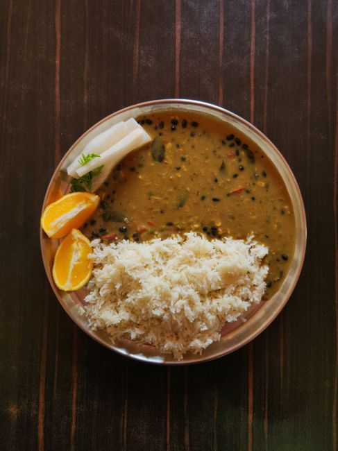 A small brass bowl of pale yellow, split moong dal next to a bowl of whole green mung beans, showing the difference between split and unsplit forms.