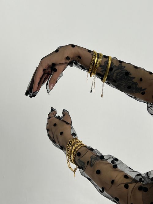 Free Tattooed hands adorned with gold bracelets, captured in a studio with stylish mesh gloves. Stock Photo