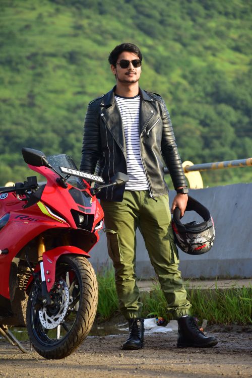 Free Man in leather jacket by sports bike with helmet in hand, set against a lush green backdrop. Stock Photo