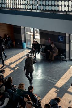 A bustling indoor terminal with people waiting and walking under bright natural light.