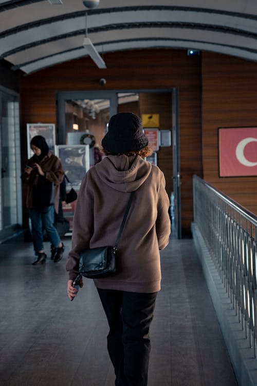 A Back View of a Woman in Brown Hoodie Walking Near the Metal Railing