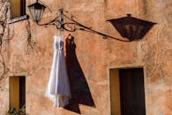 一盏华丽的罗马灯下悬挂着一件婚纱，在乡村墙壁上投下戏剧性的阴影