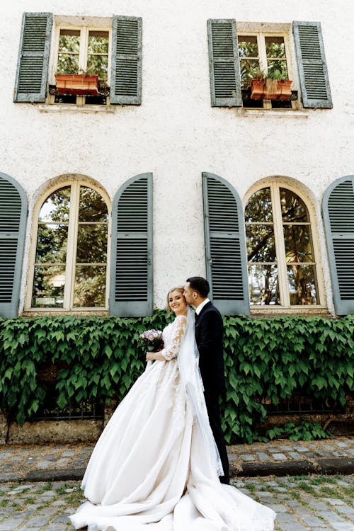 Photo of Bride and Groom Standing Near House
