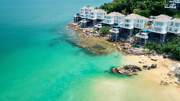 Luxury villas perched on a rocky coast with turquoise sea, offering a tropical paradise feel.