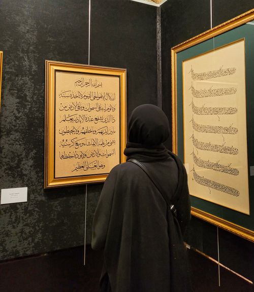 Free A woman in a hijab admires framed Arabic calligraphy in a gallery setting. Stock Photo