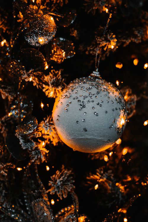 Free Close-up of a white Christmas ornament adorned with beads, surrounded by warm golden lights on a festive tree. Stock Photo