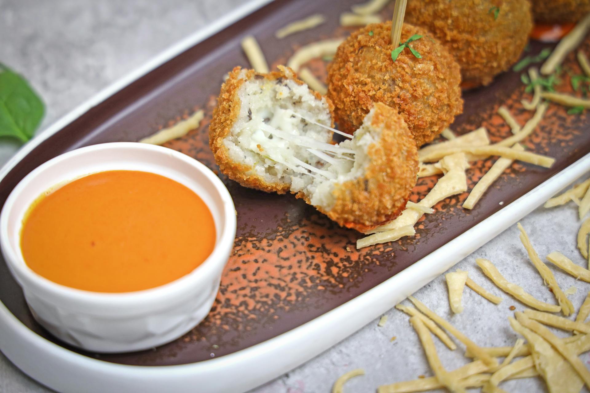 Crispy cheese croquettes served with tangy tomato dip on a decorative plate.