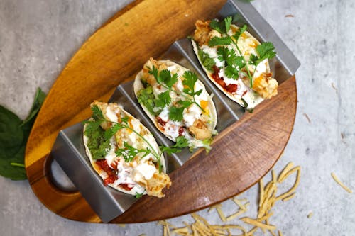 Three tacos with cheese and vegetables on a wooden cutting board