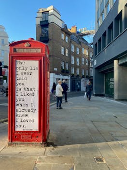 Red London telephone booth with romantic quote in an urban street setting.