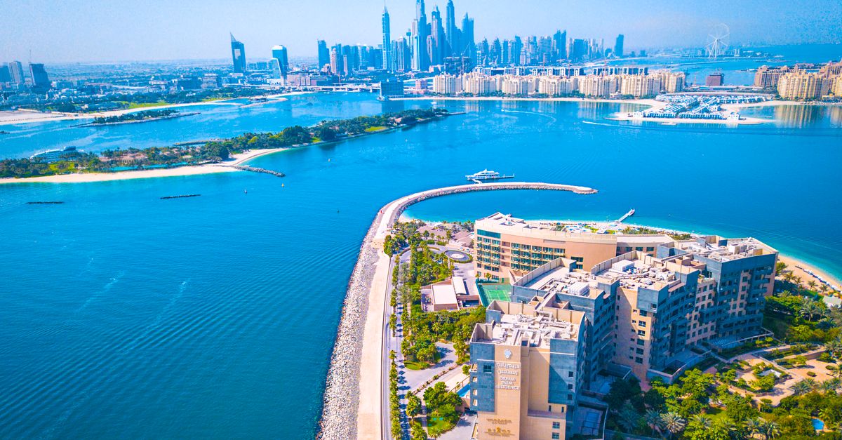 A modern UAE hospital exterior stands under a clear blue sky with palm trees in the foreground.