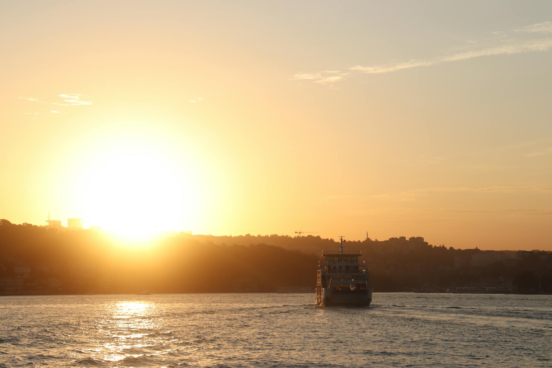 A ferry boat sails against a dramatic sunset sky, capturing serene transport over calm waters.