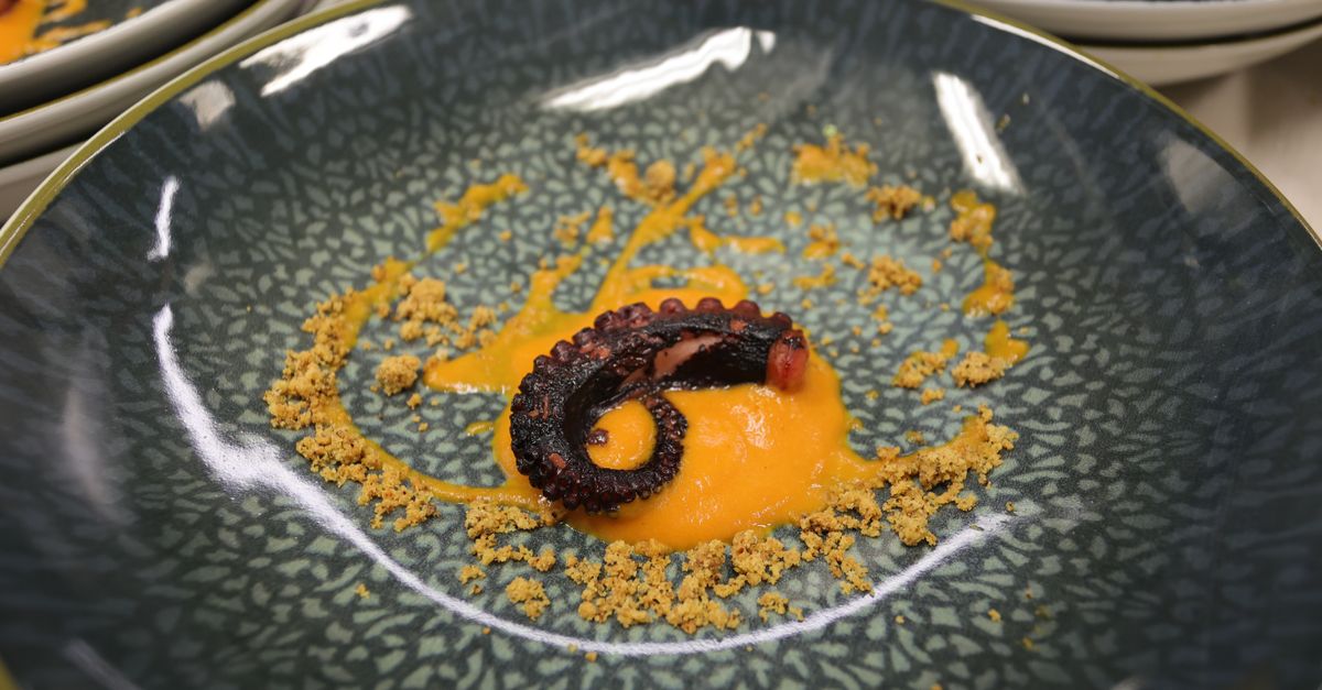 Elegant octopus tentacle on a ceramic plate with orange sauce and breadcrumbs, showcasing gourmet cuisine.
