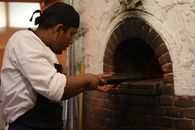 Chef sliding pizza into a rustic brick oven in a pizzeria kitchen.