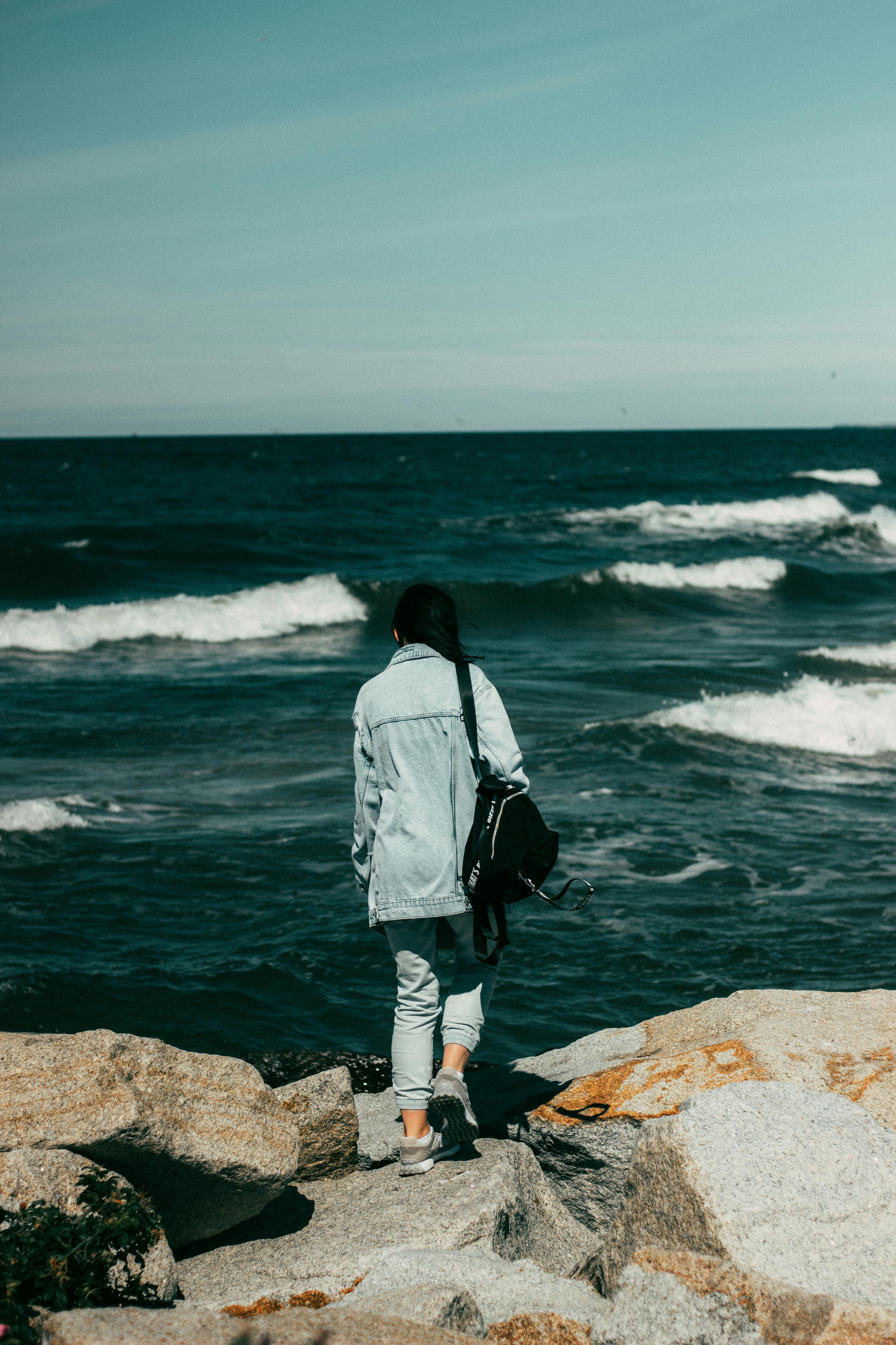 Woman stands on rocky seashore in Ustka, Poland, gazing at the ocean waves.