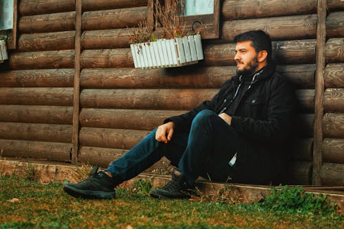 A Man in a Black Outfit Sitting Outside a Cabin
