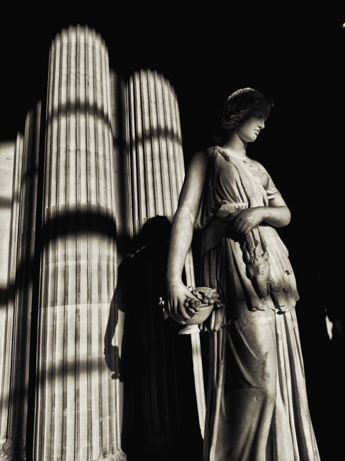 Sunlit Greek sculpture in Louvre Museum atrium with dramatic shadows.
