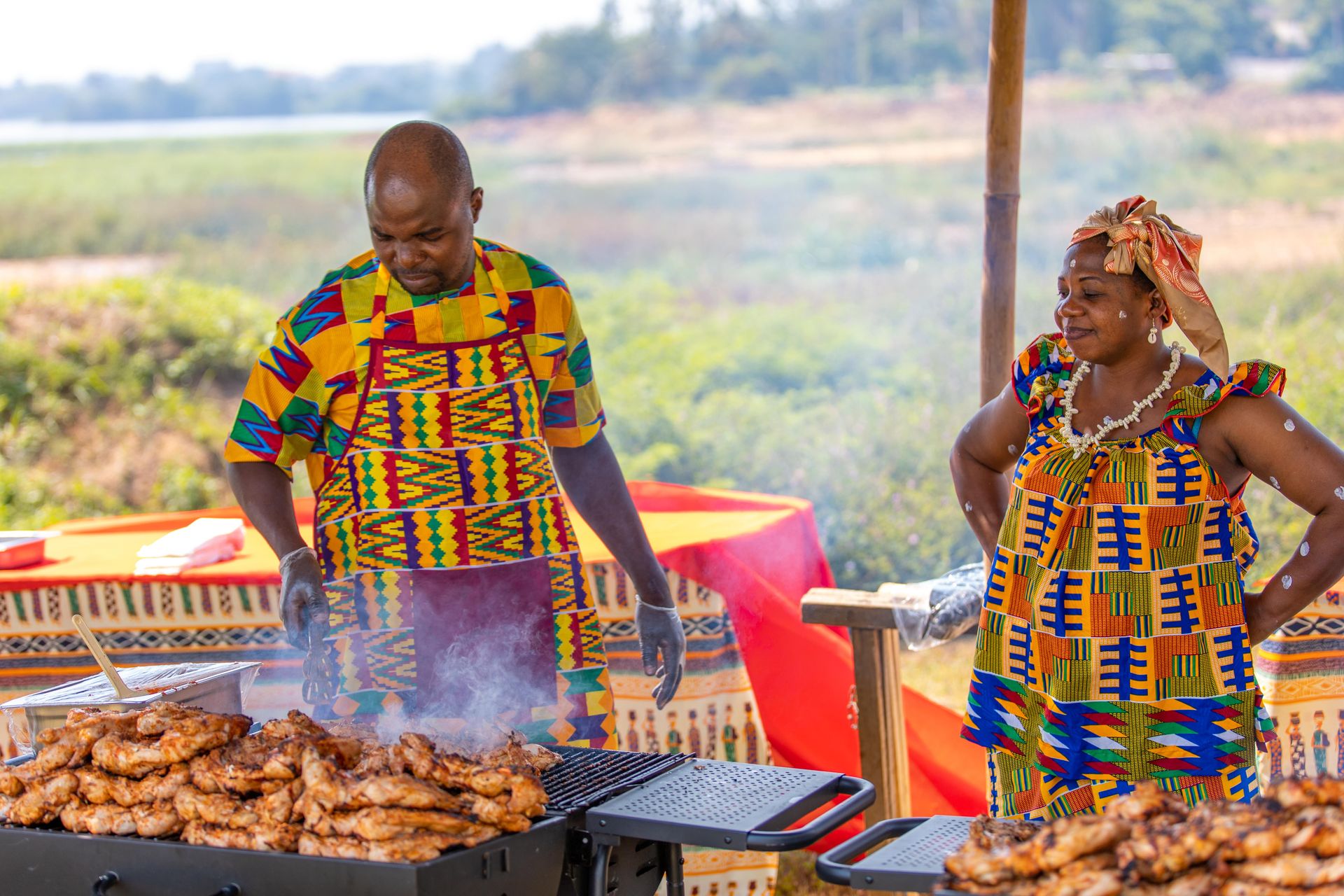Man and Woman in Traditional Clothing Grilling Meat Outdoors